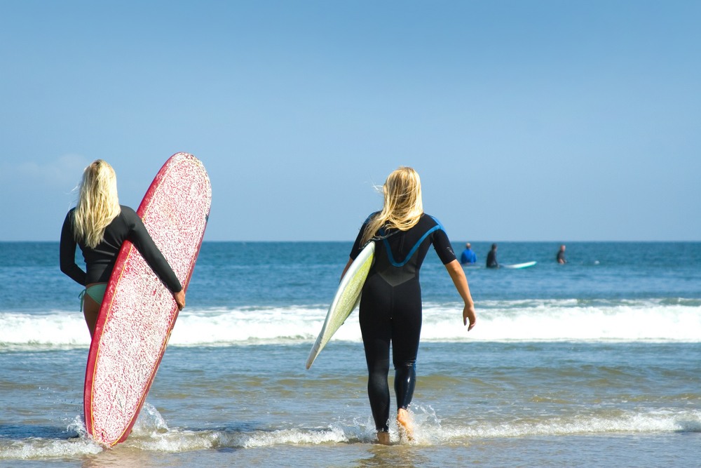 2 gals entering the water with surfboards