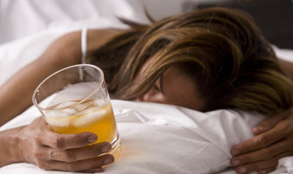 An alcoholic woman lying on her bed holding a glass of alcohol