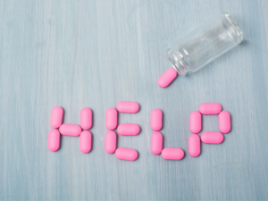 Pills spilt out of bottle that spell out the word "help" on a table.