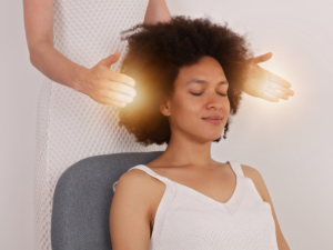Woman has hands hovering over another woman's head who looks peaceful and calm.