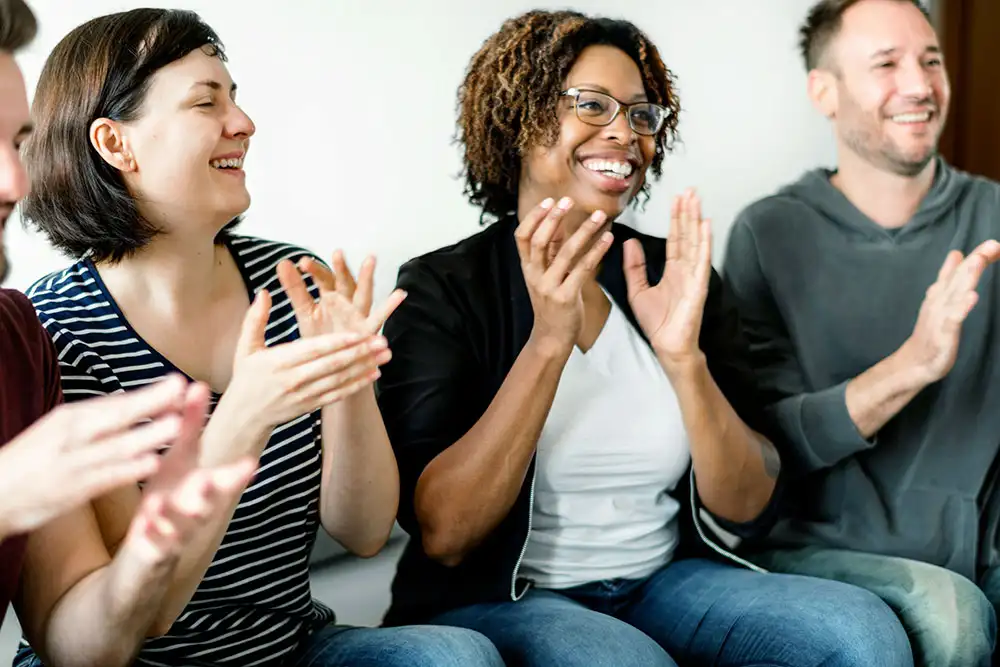 A diverse group of individuals enthusiastically clapping together, celebrating recovery at an inpatient drug rehab in Orange County, CA